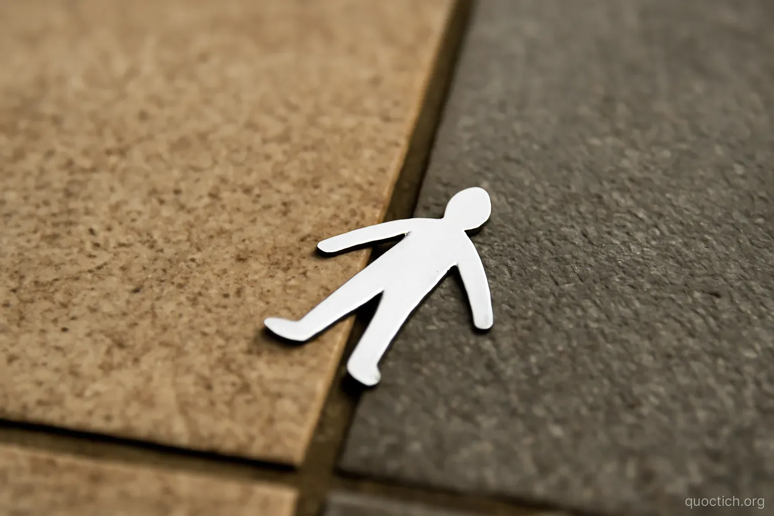 a paper cutout of a small figure lying on the seam between two different floor tiles, overhead view