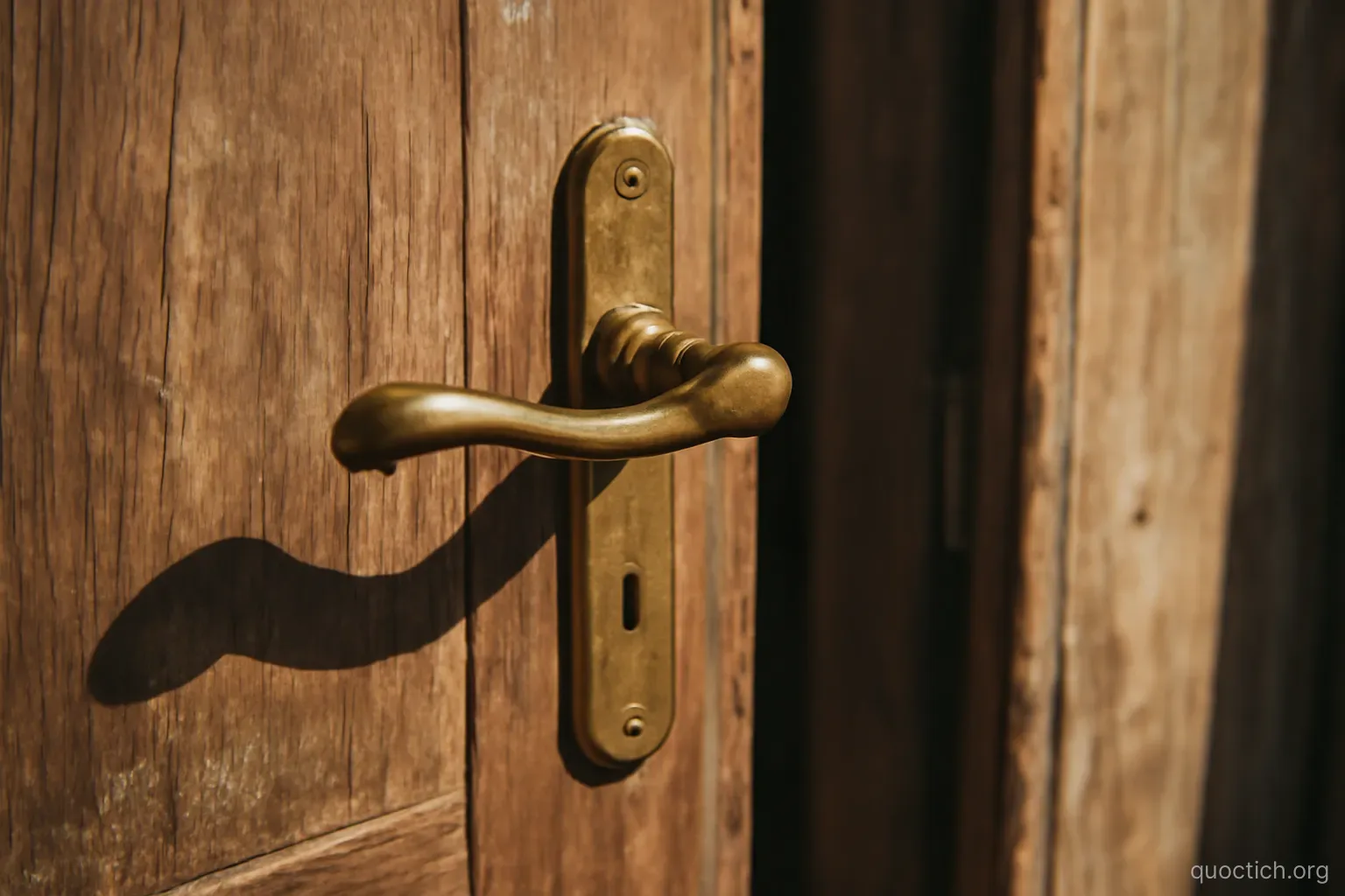 an old brass door handle on a weathered wooden door slightly open, afternoon shadow